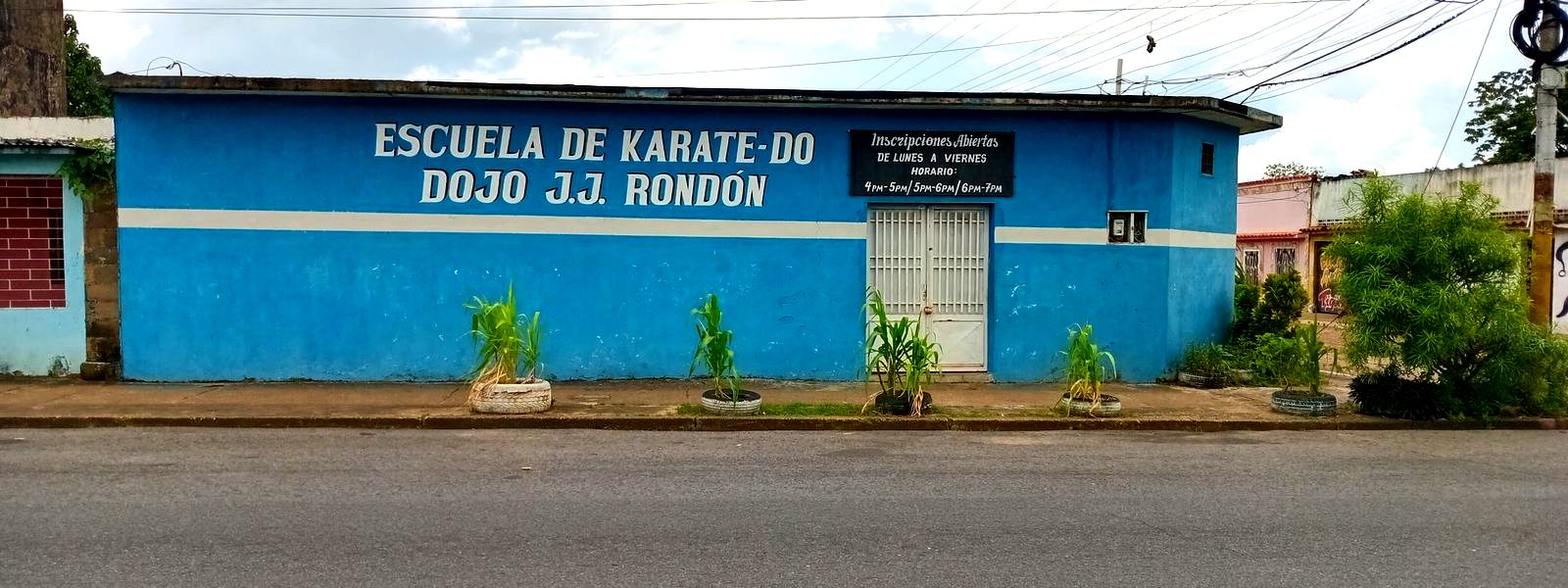 La fachada del dojo en Maturín: pared azul con el letrero Escuela de Karate-Do Dojo J.J. Rondón y un cartel de inscripciones abiertas