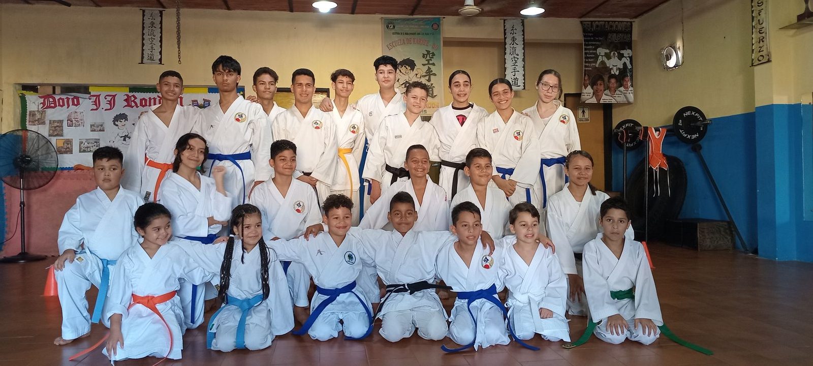 Foto de grupo del dojo: los alumnos más pequeños arrodillados adelante y los mayores de pie detrás, todos con sus cinturones