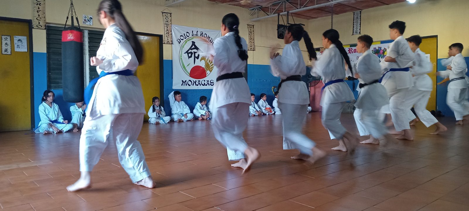Alumnos del dojo practicando desplazamientos y técnica de piernas; el movimiento deja las piernas ligeramente desenfocadas